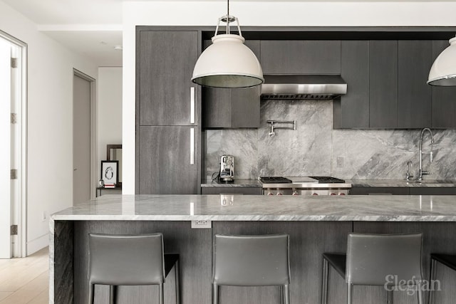 kitchen featuring wall chimney range hood, modern cabinets, a sink, and a kitchen bar