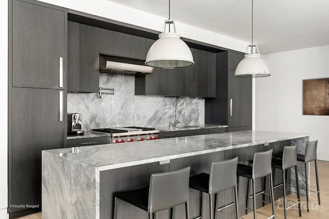 kitchen with wall chimney range hood, modern cabinets, a sink, and decorative light fixtures