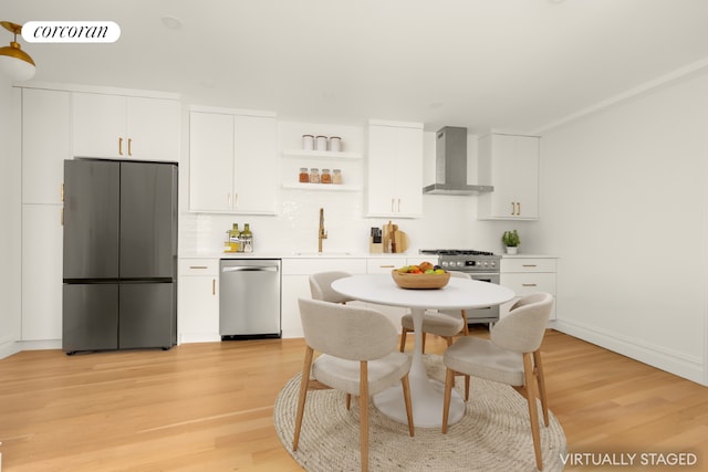 kitchen with stainless steel appliances, light countertops, white cabinets, a sink, and wall chimney range hood