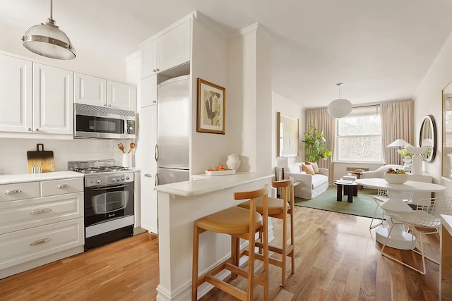 kitchen featuring premium appliances, light wood finished floors, decorative backsplash, light countertops, and ornamental molding
