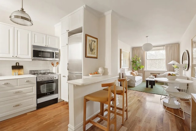 kitchen with pendant lighting, light countertops, light wood-style floors, white cabinets, and high quality appliances