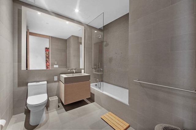 bathroom featuring tiled shower / bath, toilet, vanity, and tile walls