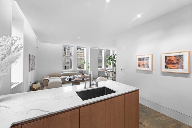 kitchen featuring brown cabinetry, modern cabinets, light stone counters, open floor plan, and a sink