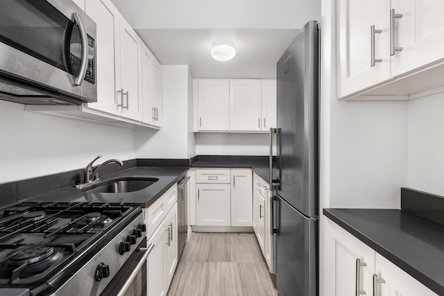 kitchen with stainless steel appliances, dark countertops, a sink, and white cabinets