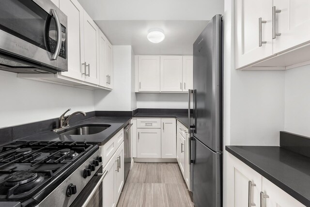 kitchen with a sink, dark countertops, appliances with stainless steel finishes, and white cabinetry