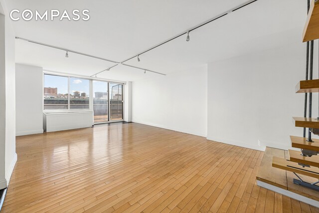 unfurnished living room featuring baseboards, track lighting, a city view, and light wood-style floors