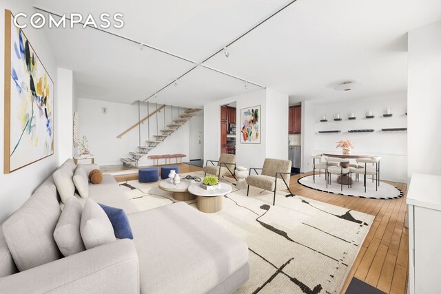 living area with light wood-style flooring, rail lighting, and stairs