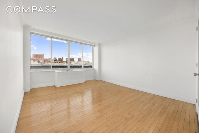 empty room with light wood-type flooring, baseboards, and a city view