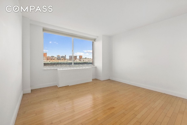 empty room featuring light wood finished floors, baseboards, and a city view