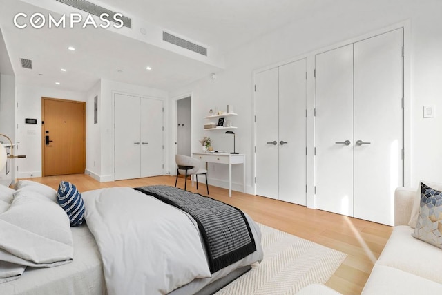 bedroom with light wood-style floors, recessed lighting, visible vents, and two closets