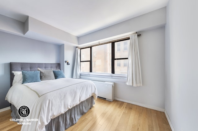 bedroom with radiator, light wood-style flooring, and baseboards