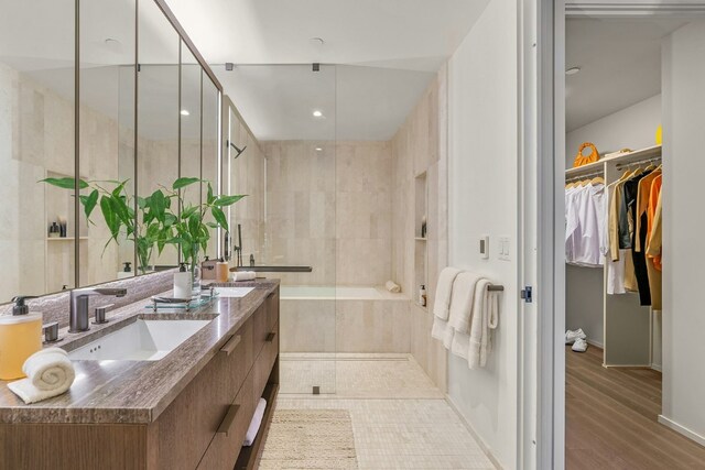 full bathroom with double vanity, tiled shower, wood finished floors, a walk in closet, and a sink