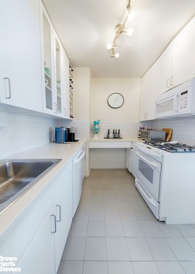 303 E 57th St Unit 32C, New York City, NY 10022 - kitchen with white cabinets, decorative backsplash, glass insert cabinets, white appliances, and light tile patterned floors