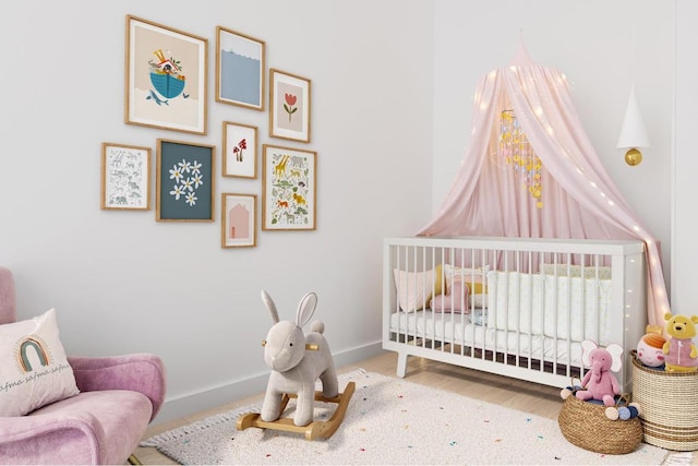 bedroom with a nursery area, baseboards, and wood finished floors