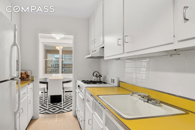 kitchen with under cabinet range hood, white appliances, white cabinetry, and a sink