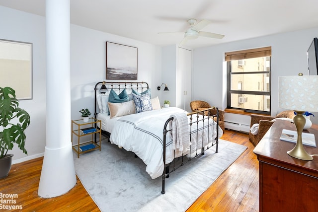 bedroom featuring ceiling fan, a baseboard radiator, baseboards, wood-type flooring, and decorative columns