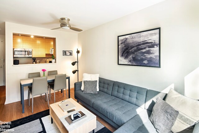 living area with a ceiling fan, baseboards, and wood finished floors