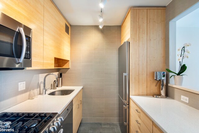 kitchen with tile walls, stainless steel appliances, light brown cabinetry, a sink, and modern cabinets