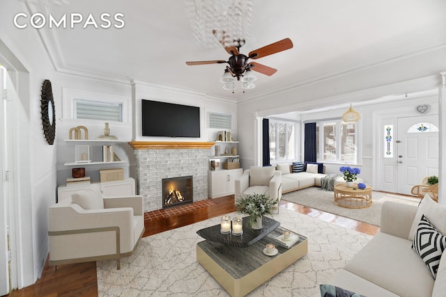 living area featuring ceiling fan, a fireplace, wood finished floors, and crown molding