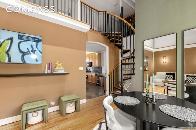 dining space featuring arched walkways, baseboards, a towering ceiling, light wood-style flooring, and stairway