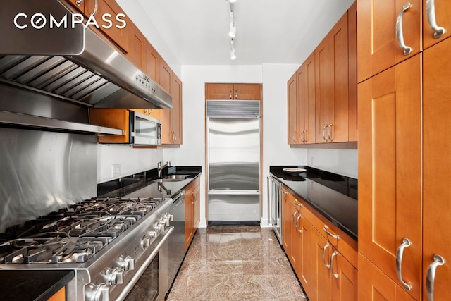 kitchen with dark countertops, appliances with stainless steel finishes, brown cabinets, ventilation hood, and granite finish floor