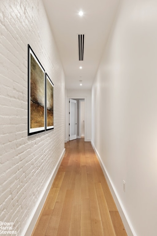 corridor with brick wall, recessed lighting, wood finished floors, and baseboards