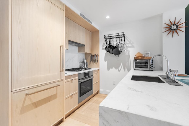 kitchen featuring appliances with stainless steel finishes, light brown cabinets, a sink, and light wood-style flooring