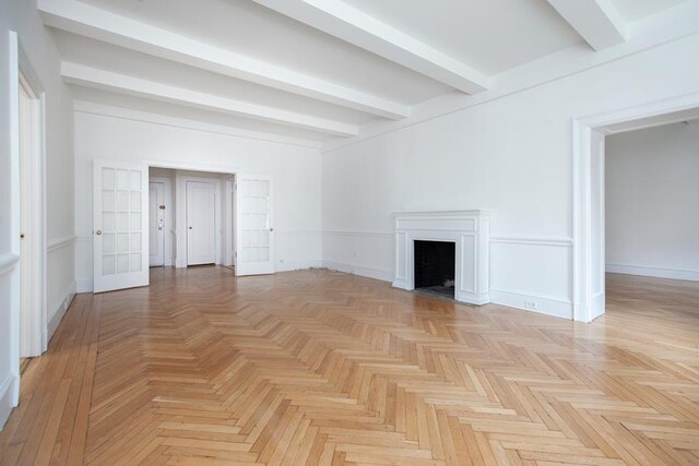 21 E 66th St Unit 4-E, New York City, NY 10065 - unfurnished living room featuring a fireplace, baseboards, beamed ceiling, and french doors
