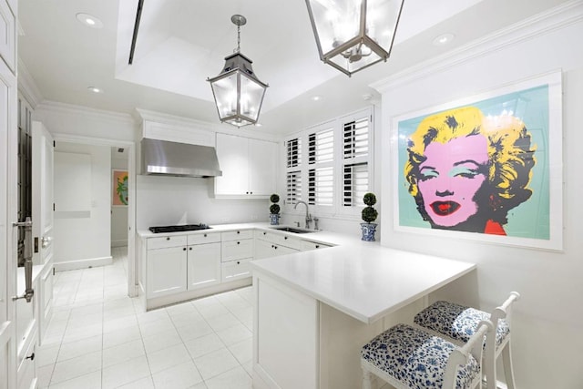 kitchen with light countertops, white cabinetry, a sink, a peninsula, and wall chimney exhaust hood