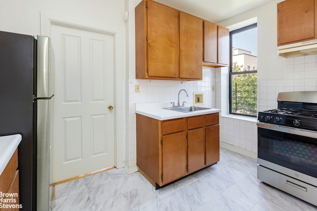 kitchen featuring under cabinet range hood, stainless steel appliances, a sink, marble finish floor, and light countertops