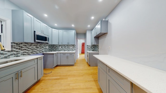 kitchen with stainless steel microwave, light wood finished floors, a sink, decorative backsplash, and light countertops