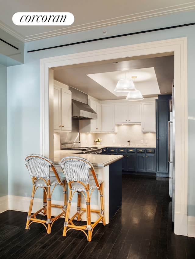 180 E 93rd St Unit 2, New York City, NY 10128 - kitchen featuring a raised ceiling, dark wood finished floors, wall chimney range hood, white cabinets, and a breakfast bar