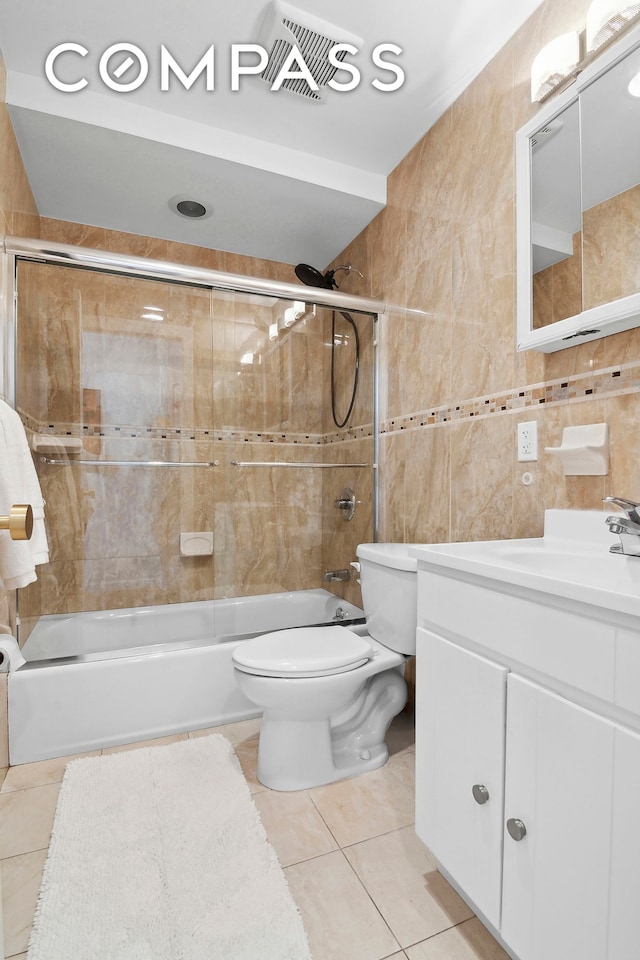 bathroom featuring tile patterned flooring, vanity, toilet, tile walls, and bath / shower combo with glass door