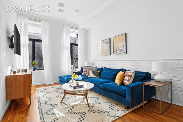 living area with visible vents, ornamental molding, baseboards, and wood finished floors