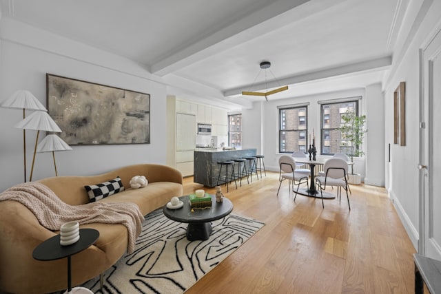 living area with baseboards, beam ceiling, and light wood-style floors