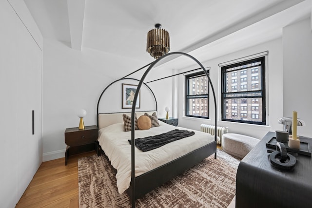 bedroom with radiator, light wood-type flooring, a chandelier, and beamed ceiling