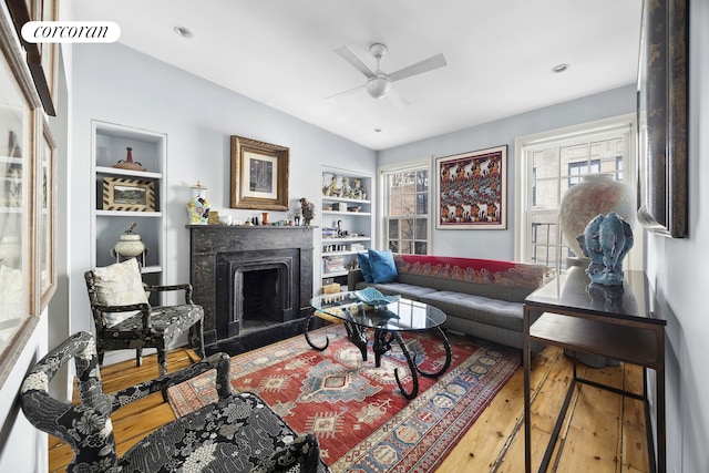 living room with ceiling fan, hardwood / wood-style floors, a fireplace, and built in features