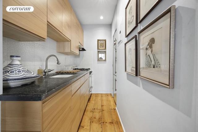 kitchen with light brown cabinets, decorative backsplash, a sink, and light wood-style floors