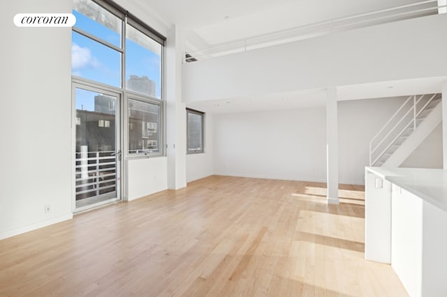 spare room with visible vents, baseboards, a towering ceiling, light wood-style flooring, and stairs