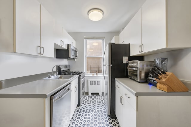 kitchen featuring appliances with stainless steel finishes, a sink, white cabinetry, and light floors