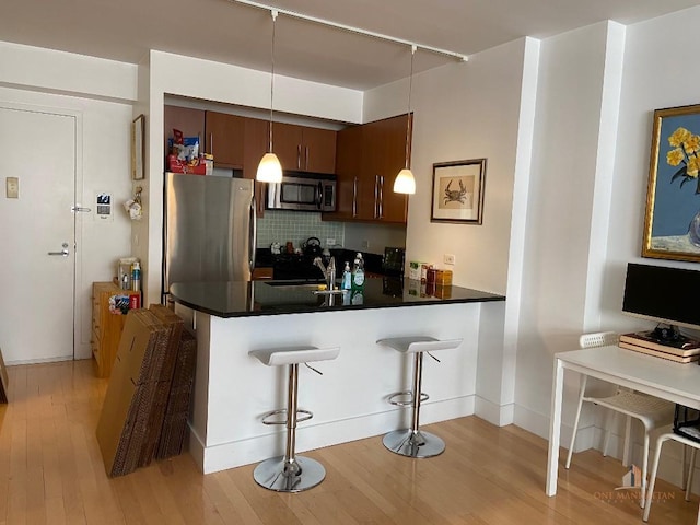 kitchen featuring stainless steel appliances, hanging light fixtures, a sink, a peninsula, and a kitchen breakfast bar