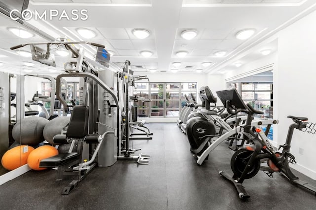 exercise room featuring a paneled ceiling and baseboards