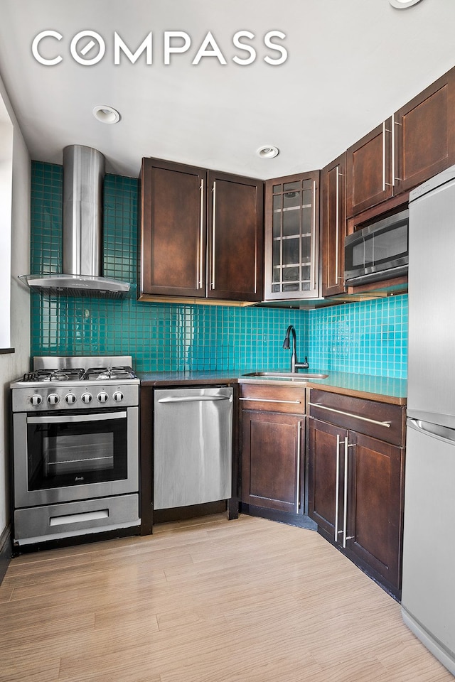 kitchen with a sink, appliances with stainless steel finishes, wall chimney exhaust hood, and dark brown cabinets