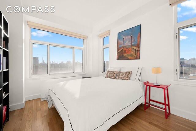 bedroom featuring a view of city, multiple windows, baseboards, and wood finished floors