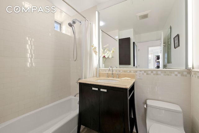 bathroom with tile walls, visible vents, toilet, shower / bath combo with shower curtain, and vanity