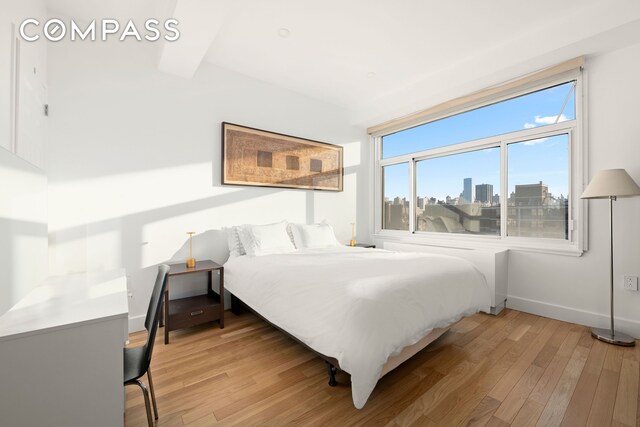 bedroom with light wood-style floors, baseboards, and a city view