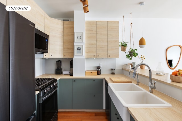 kitchen with freestanding refrigerator, gas range oven, light countertops, pendant lighting, and a sink