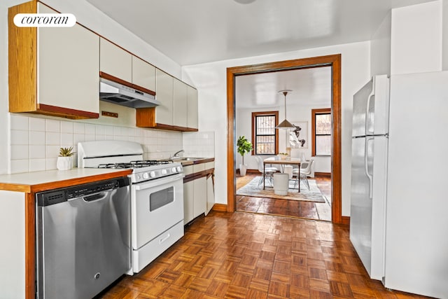 kitchen with white appliances, decorative backsplash, light countertops, under cabinet range hood, and white cabinetry