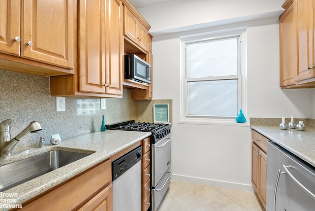 kitchen with light stone countertops, a sink, baseboards, appliances with stainless steel finishes, and decorative backsplash