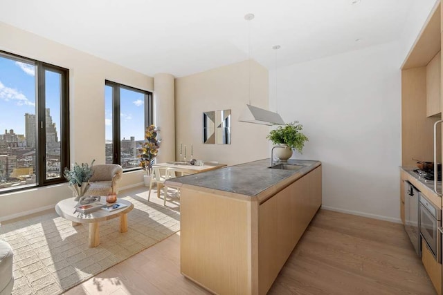 kitchen with pendant lighting, a city view, light wood-style flooring, light brown cabinets, and a sink